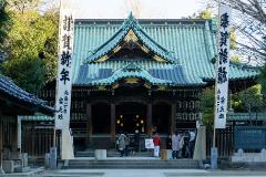 A serene Japanese temple is adorned with lanterns and banners, drawing visitors to its entrance on a bright day.