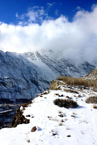 Snow-covered mountain landscape with clouds covering the peaks and animal tracks visible on the ground.