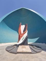 The Martyrs' Monument in Baghdad, Iraq, features a draped flag sculpture set against a blue, tiled, dome-like structure, creating a striking and symbolic tribute.