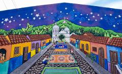 Colorful mural of a street leading to a church on a hill under a starry night, adorned with people and carpets on cobblestone street.