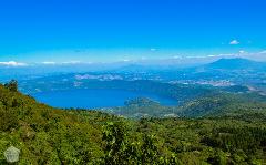 A scenic view of a lake surrounded by lush green hills and mountains under a clear blue sky.