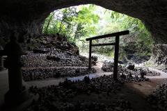 An interesting cave with a Japanese Torii gate, small piles of stones, and a stone lantern on the left.
