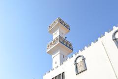 A white building with a tall, ornate tower stands against a clear blue sky.