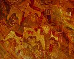 The image displays ancient rock art, likely depicting stylized animals and symbols, in warm earth tones on a rough, textured surface, evoking a sense of history and cultural heritage.