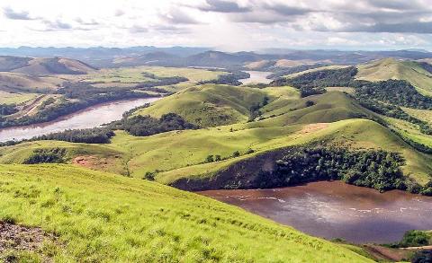 A wide shot of a winding river flowing through lush green hills and valleys under a cloudy sky.