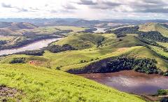 A wide shot of a winding river flowing through lush green hills and valleys under a cloudy sky.