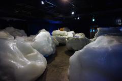 A dark room with many white, rounded objects that look like icebergs and an orange-brown animal standing on top of them.