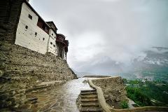A stone pathway leads up to a white building perched on a hill, with misty mountains in the background.