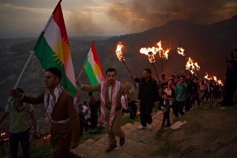 Eine Menschenmenge mit kurdischen Flaggen und Fackeln marschiert in der Abenddämmerung einen Hügel entlang.