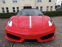 The image features a red Ferrari sports car parked in front of a building named "Chaucer House" with a well-maintained green hedge in the background.