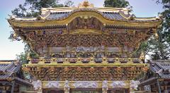 A highly ornate and gilded Japanese temple facade with intricate carvings, statues, and a multi-tiered roof set against a backdrop of trees.