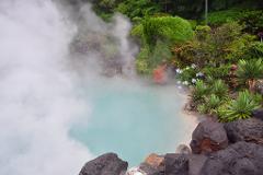 A turquoise pool surrounded by lush greenery and volcanic rocks, with steam rising from the water, creating a mystical atmosphere.