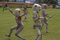 A group of people in costumes and masks are seen performing a traditional dance or ritual in a grassy field at the Goroka Show Festival in Papua New Guinea.