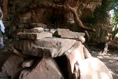 A stone altar stands in front of a cave, with rocks stacked on top of each other and a tree branch extending over the scene.