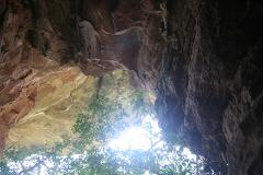 A low-angle shot of a rocky overhang reveals a glimpse of bright sunlight and foliage.