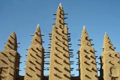 The image showcases the striking architecture of the Grand Mosque of Djenné in Mali, featuring its distinctive mud-brick towers and timber supports against a clear blue sky.