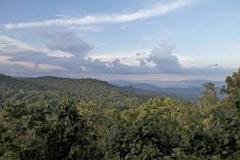 Here's a description of the image:The image showcases a lush, green mountain landscape under a sky with scattered clouds, likely taken near Bukavu, possibly overlooking lakes and lowland gorilla habitat.