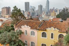 Gran Tour incluyendo Bogotá, Medellín, Nuquí y Valle del Cocora - 11 Días A cityscape view with pink and yellow buildings featuring arched windows and terracotta roofs in the foreground, set against a backdrop of modern skyscrapers under a cloudy sky.