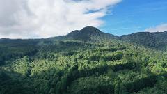 A lush, green mountainous landscape with a cloudy blue sky.