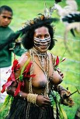 Here is a description of the image:A woman in traditional attire with face paint, bead necklaces, and a feathered headdress poses at the Mt. Hagen Festival in Papua New Guinea, showcasing cultural elements and body adornments.
