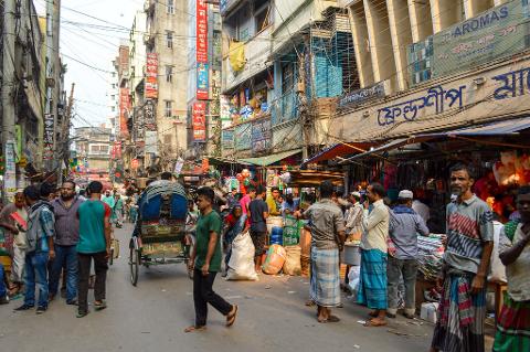 3-Day Dhaka Heritage & Culture Tour — Old Palaces, Lost Cities & Zamindari Mansions A crowded street market in Dhaka, Bangladesh, with people and rickshaws navigating between stalls laden with goods.