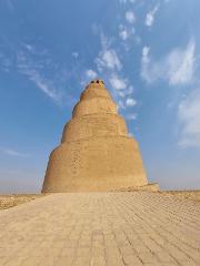 A spiraling ziggurat-style brick tower rises against a partly cloudy blue sky.