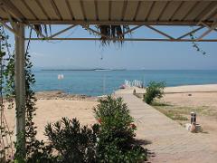 A scenic view of a tranquil beach and turquoise sea framed by a covered walkway with lush greenery.