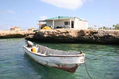 A white boat with Arabic writing floats in the turquoise water in front of a rocky island with a white building.