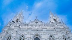 A low-angle shot of the Immaculate Conception Cathedral, a stunning white Gothic Revival church with intricate details, set against a bright blue sky.