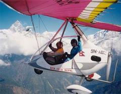 Two people are flying in an ultralight aircraft with the Annapurna mountain range in the background.
