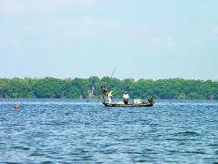 Ciénaga Grande de Santa Marta Birdwatching from Santa Marta Three people are on a small boat in the water, with trees in the background and a buoy in the water to the left of the boat.