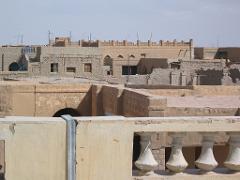 A view from a rooftop, showing interconnected buildings and structures with a mix of sandy-colored brickwork, arches, and weathered details against a clear sky.