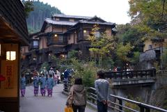 A street scene in a Japanese town with traditional buildings, a bridge, and people walking around.