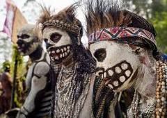 Here's a one-sentence description of the image:Three people in elaborate tribal costumes and face paint, resembling skeletal figures with prominent teeth, are part of the Mt. Hagen Festival in Papua New Guinea.