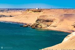 A scenic view of Angola's desert coastline with cliffs, sandy beaches, and turquoise waters under a clear blue sky.