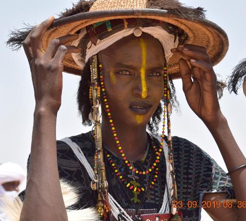 A man with traditional face paint and a straw hat poses for a close-up shot, showcasing cultural attire and accessories.