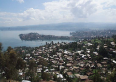 Dies ist eine Landschaftsansicht einer Stadt auf einem Hügel in der Nähe eines Sees mit bewölktem Himmel, die dem Seitentitel zufolge möglicherweise in der Demokratischen Republik Kongo oder in Ruanda aufgenommen wurde.