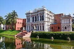 A picturesque palace with intricate white detailing sits beside a tranquil canal, partially covered in scaffolding, reflecting in the water under a clear blue sky.