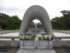 The Hiroshima Peace Memorial, with a gray arch framing the Atomic Bomb Dome, is adorned with colorful flowers in the foreground.