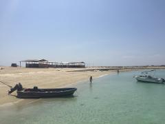 A serene beach scene with clear water, boats, and a few people enjoying the calm day.