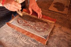 A person is using a brush to apply pigment through a stencil onto a piece of fabric, possibly in a textile printing or dyeing process.