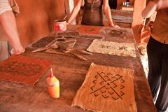 A table covered in various patterned fabrics and tools, with three people standing around it.