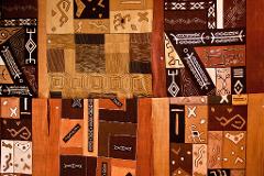This image shows a colorful, patterned textile featuring geometric shapes and abstract tribal-inspired designs in shades of brown, beige, and white.