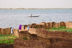 A person is in a boat on a river by some straw fences with laundry hanging on them.
