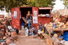 A woman shops at a red pottery stand surrounded by a group of children and various clay pots.