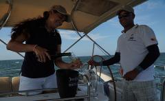 Cultural Caribbean Tour A woman pours champagne into a glass on a boat, while a man stands nearby at the wheel.