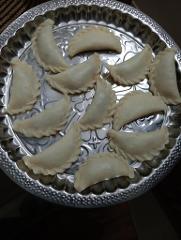 A silver platter is filled with several crescent-shaped dumplings with crimped edges.