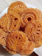 A close-up shot shows a plate piled high with intricately designed, golden-brown, round pastries, showcasing detailed leaf and floral patterns.