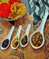 A close-up shot showcasing four white spoons filled with different types of sweet or savory toppings, placed on a golden decorative surface with a bowl of flowers in the background.