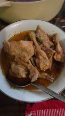 A bowl of chicken curry with gravy and a spoon, placed on a table with a red and white striped cloth.